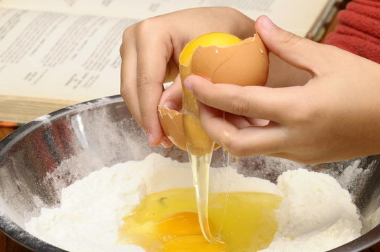 儿童手把鸡蛋打入面粉和食谱的背景