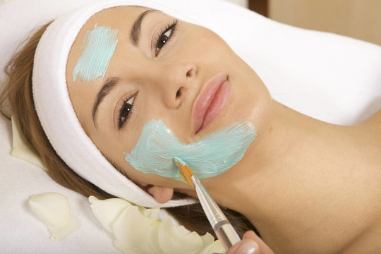 年轻女人用刷子在脸上得到美容面膜