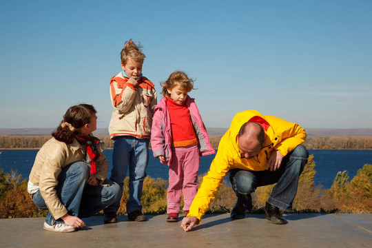 从四人走在太阳秋天的家庭。父母在沥青上画粉笔。