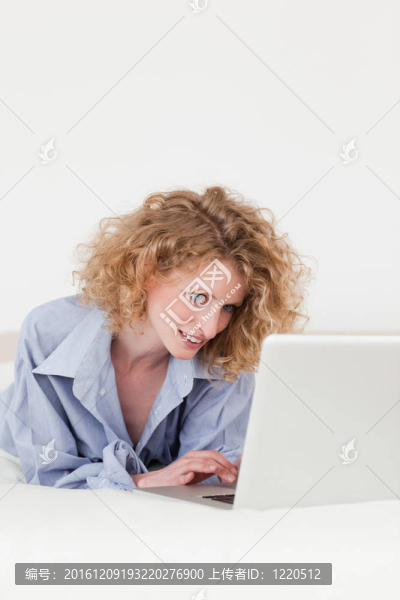 漂亮的金发女放松她的笔记本电脑在她的公寓里躺在自己的床上