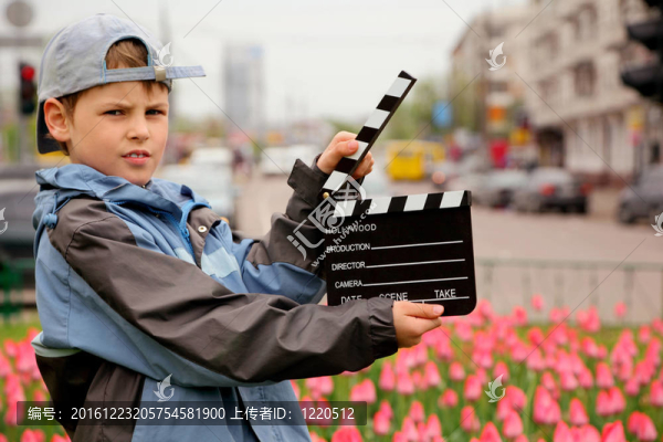 一个男孩在夹克和帽子电影拍板在手站在郁金香田野在城市的街道